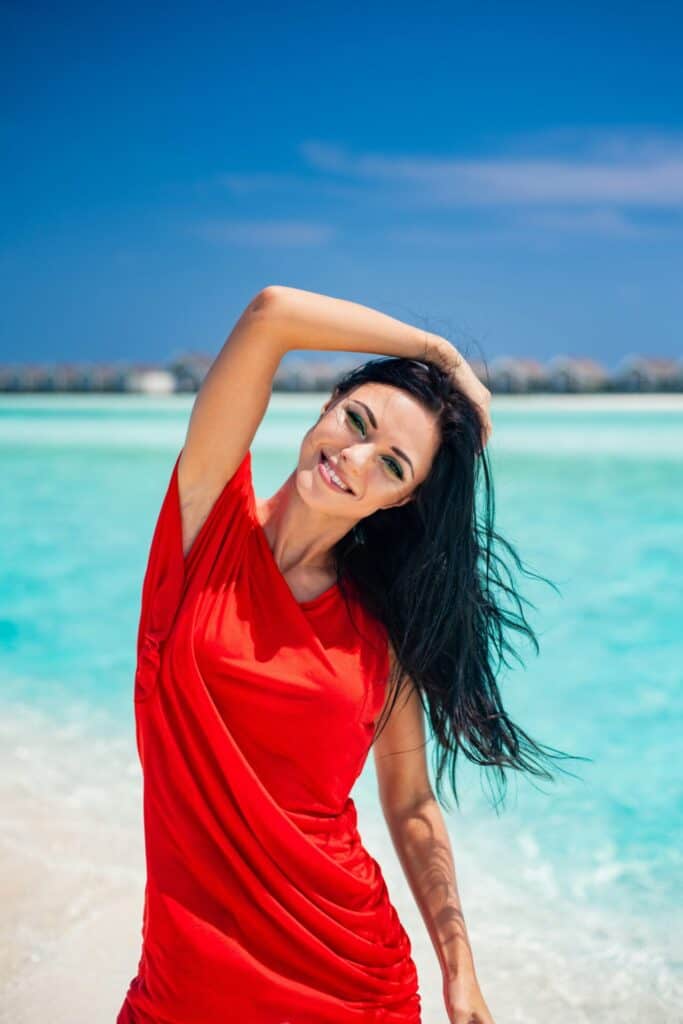 Frau im roten Kleid vor dem blauen Meer stehend