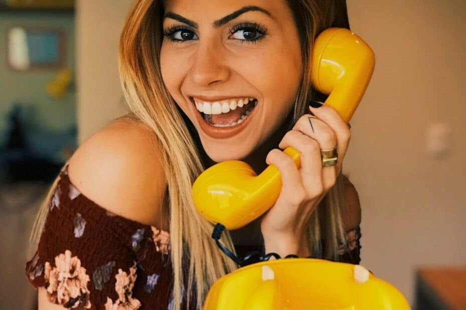 Sympathische Frau an einem alten, gelben Schnurtelefon als erster Kontakt im Escort Casting.
