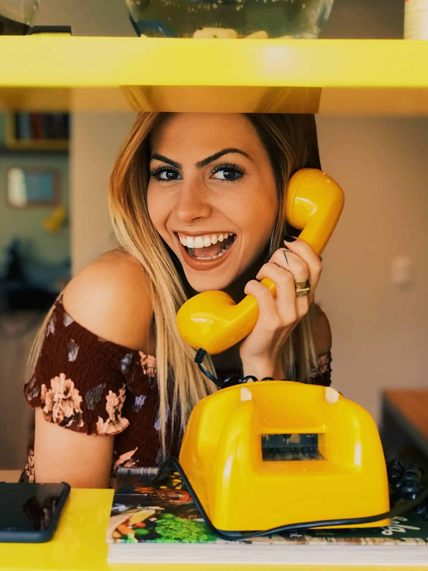 Sympathische Frau an einem alten, gelben Schnurtelefon als erster Kontakt im Escort Casting.