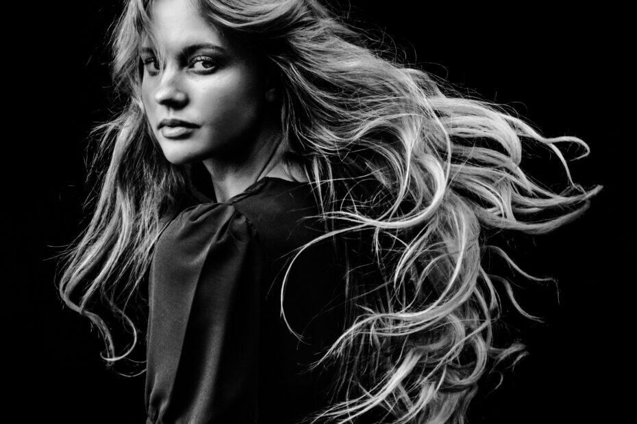 Coverbild zum Artikel über Royale Escort aus München. Gezeigt wird eine junge Frau mit langen Haaren in schwarzer Kleidung, die ihren Kopf nach hinten dreht und so in die Kamera schaut.