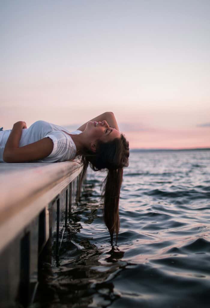 Diary Lady Escort auf einen Pier liegend mit dem Zopf im Wasser.