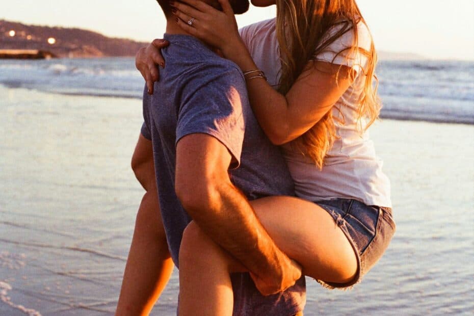 Coverbild zum Artikel über Never Forget Escort mit einem verliebten, sich küssenden Paar am Strand, wobei der Mann die Frau trägt und sie ihre Beine um ihn schlingt.